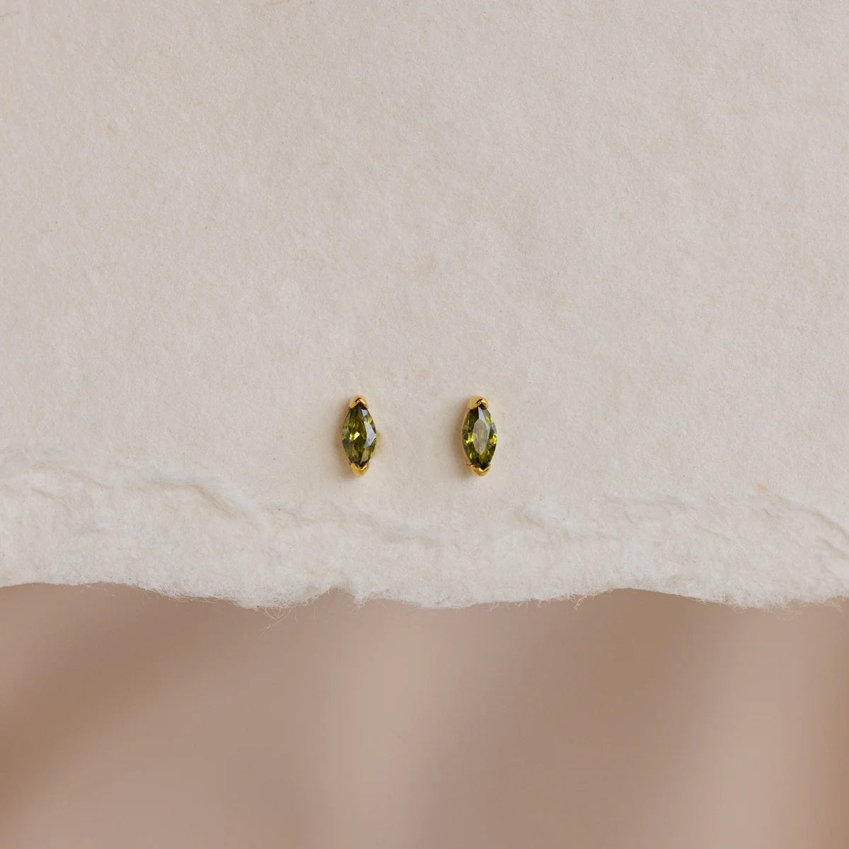 Pair of gold earrings with green gemstones on a white fabric background