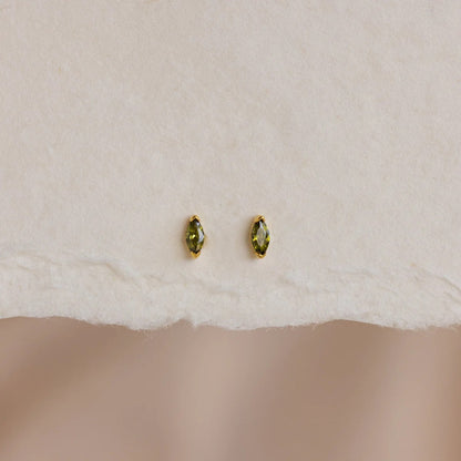 Pair of gold earrings with green gemstones on a white fabric background