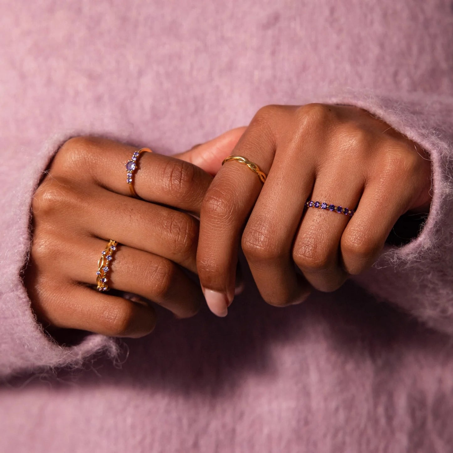 Close-up of two hands wearing rings on a pink background