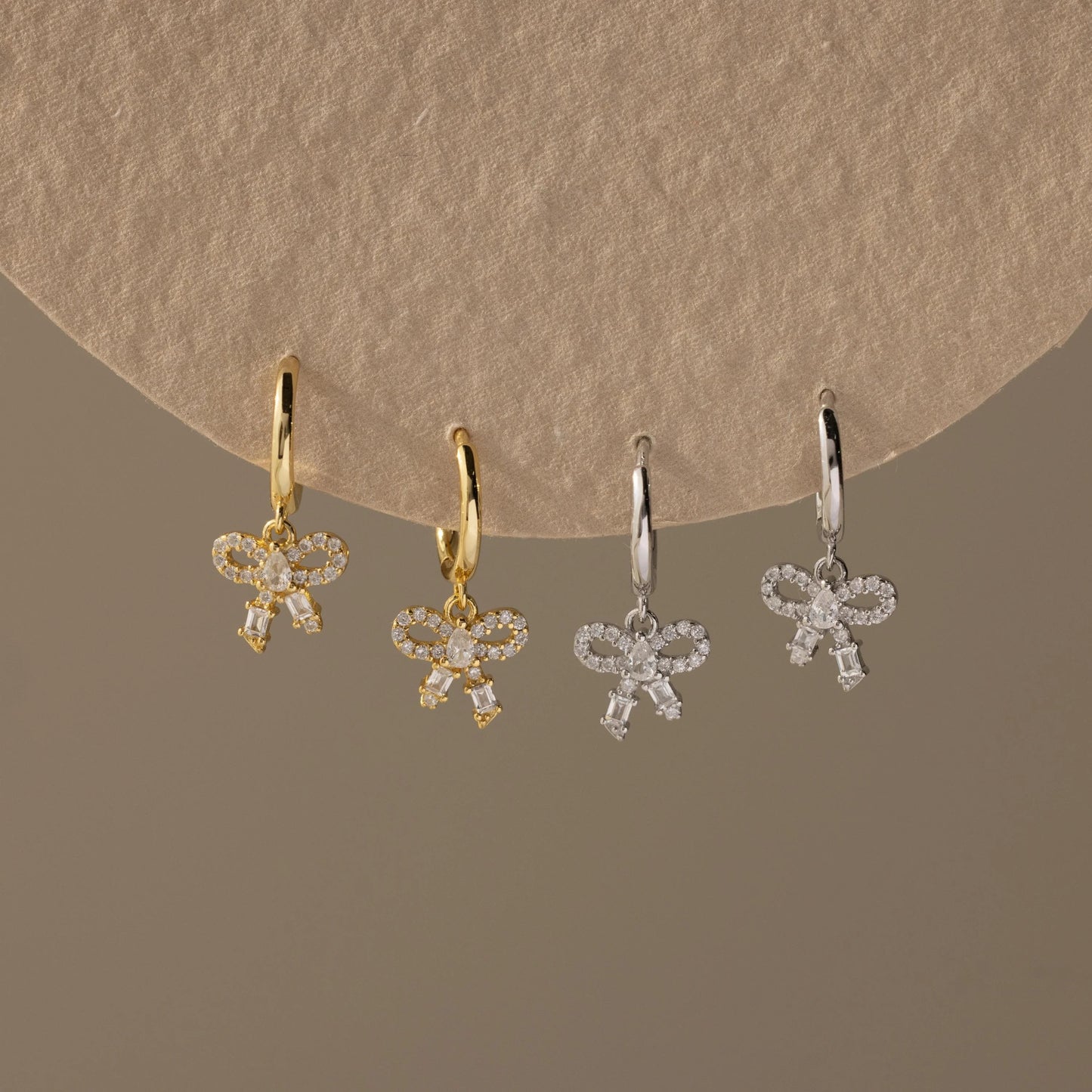Four pairs of bow-shaped earrings in gold and silver on a beige background