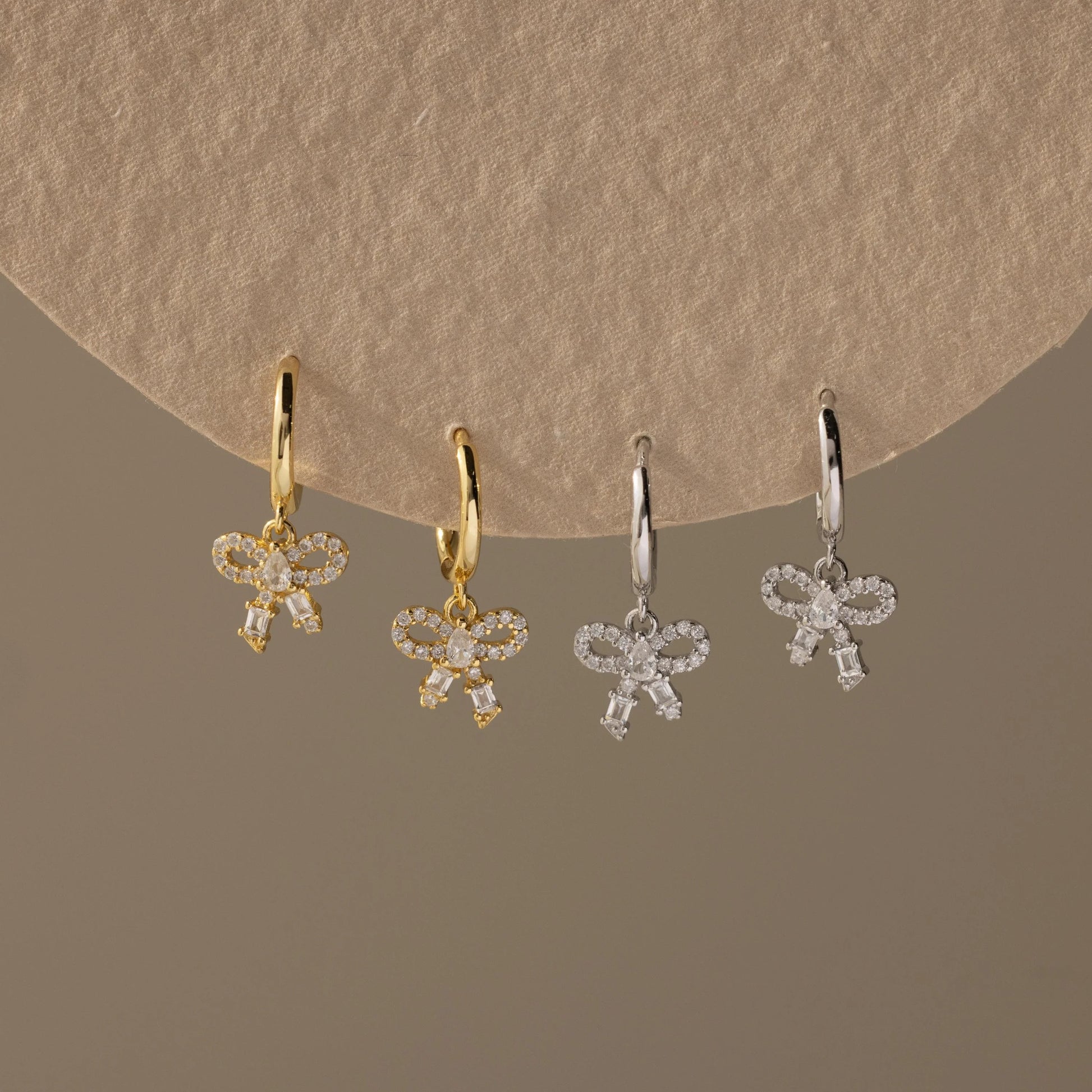 Four pairs of bow-shaped earrings in gold and silver on a beige background