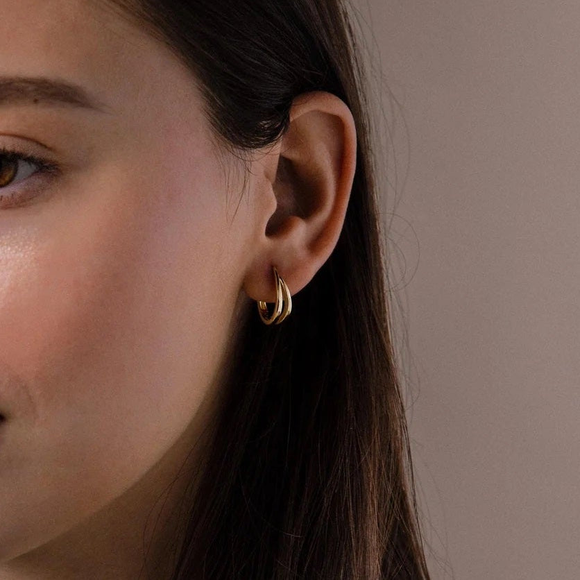 Close-up of a woman with long dark hair wearing a gold earring against a neutral background
