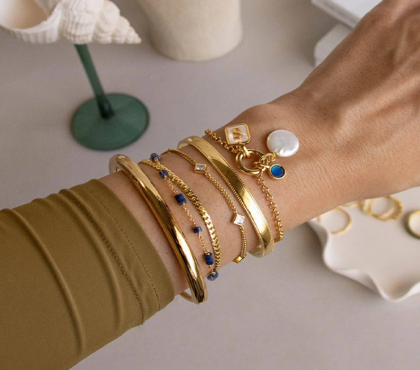 Close-up of a wrist wearing multiple gold bracelets with various charms on a neutral background.