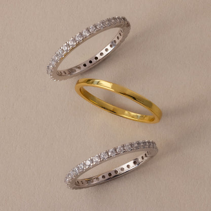 Two diamond eternity rings, one gold and one silver, on a beige background.