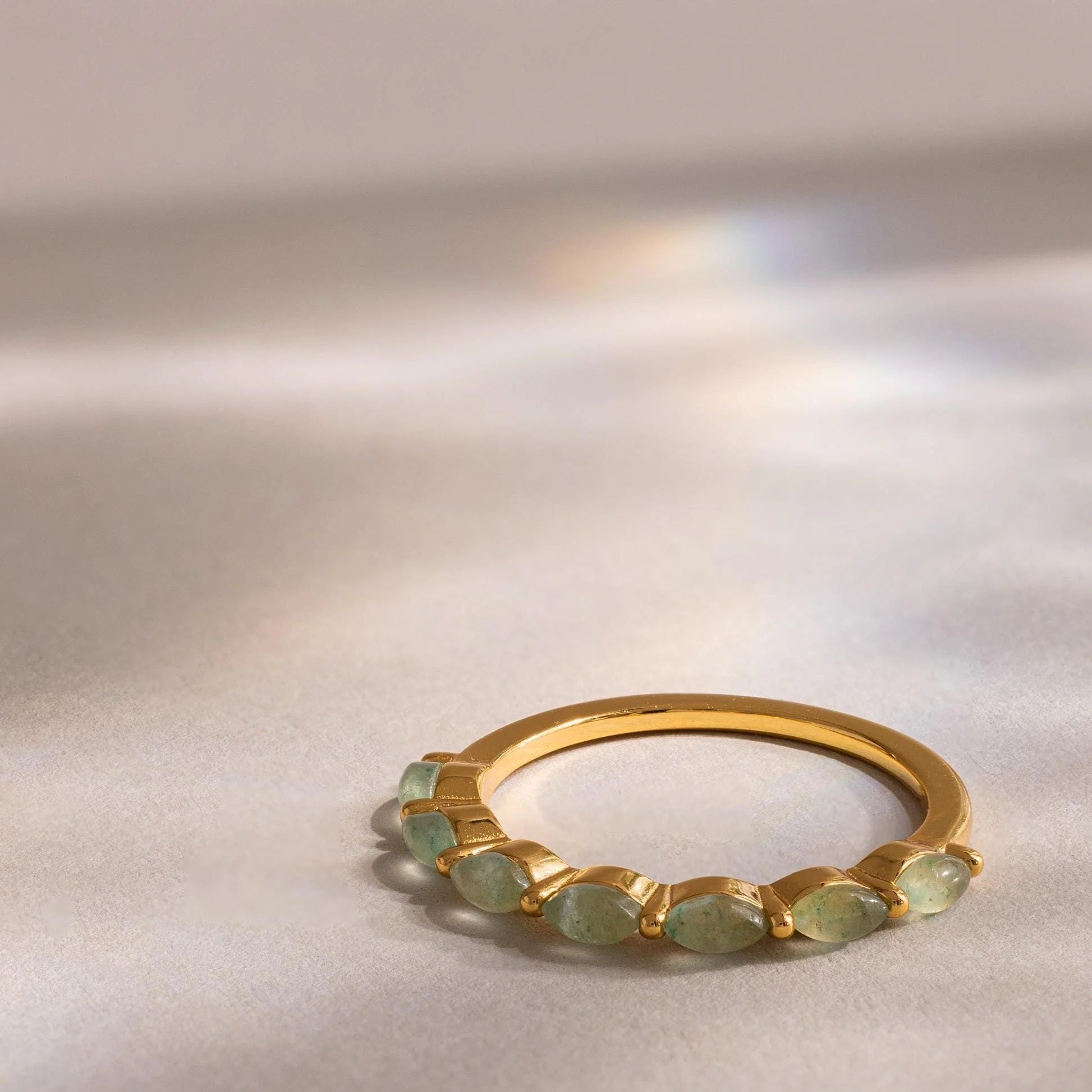 Gold ring with green gemstones on a reflective surface