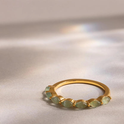 Gold ring with green gemstones on a reflective surface