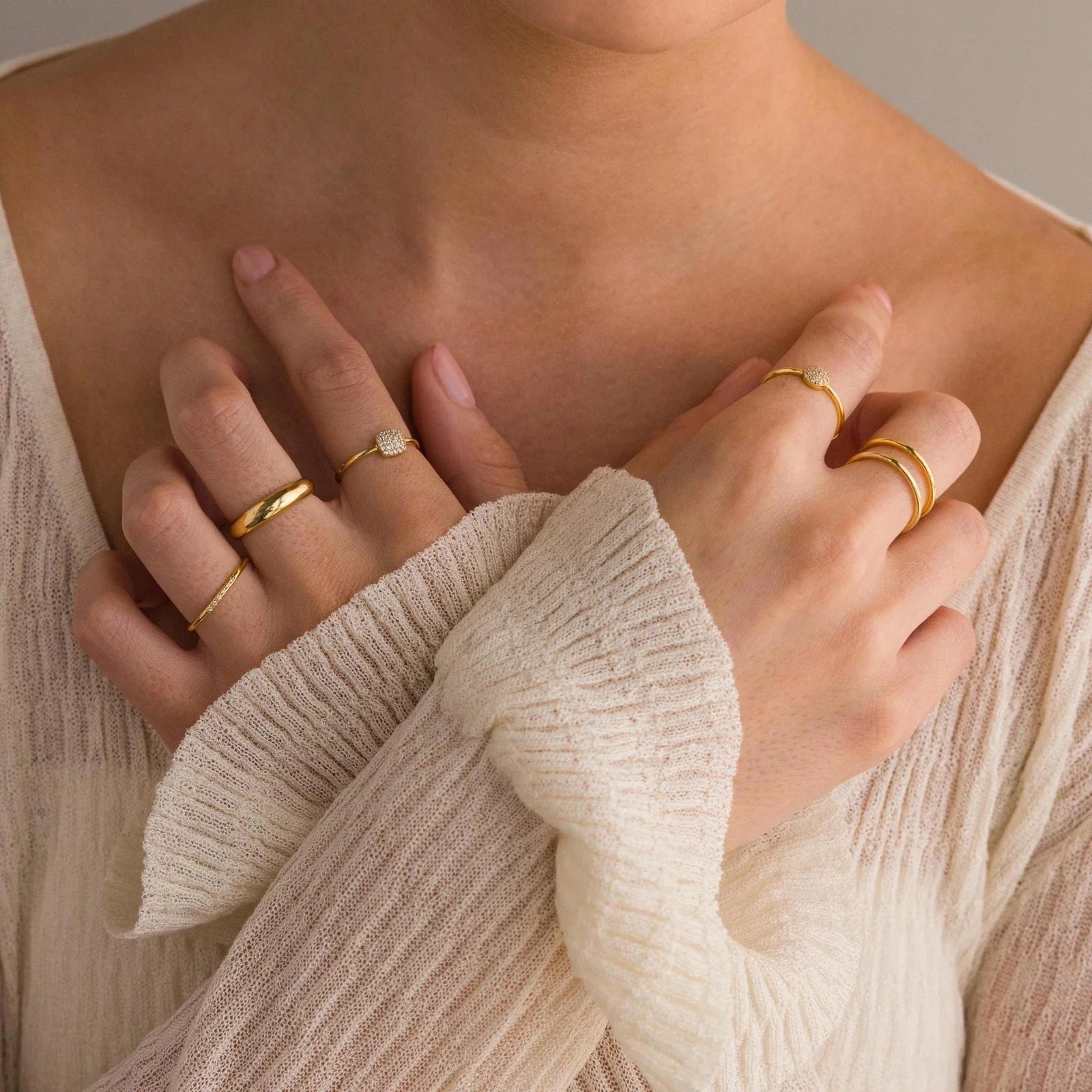 Close-up of hands wearing gold rings on a neutral background