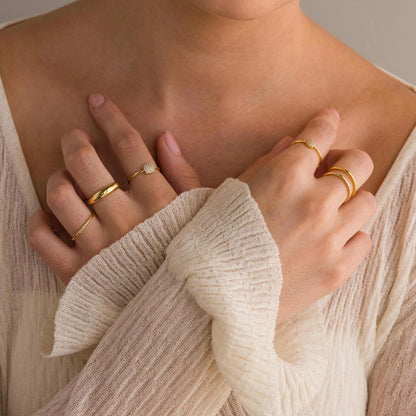 Close-up of hands wearing gold rings on a neutral background