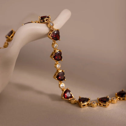 Gold bracelet with heart-shaped gemstones on a mannequin hand against a neutral background