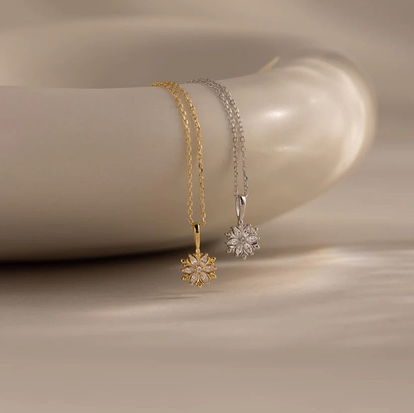 Two gold and silver snowflake-shaped pendants on a neutral background