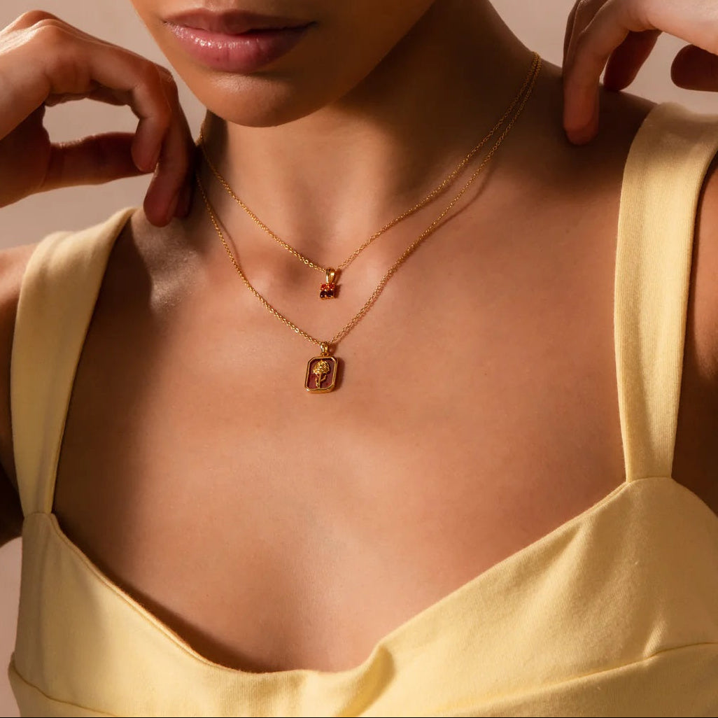 Woman wearing a gold necklace with a pendant against a neutral background