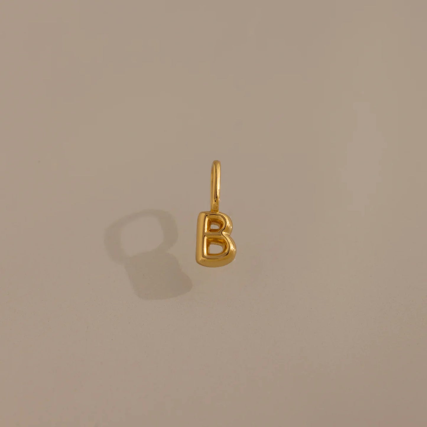 Gold letter 'B' charm on a beige background