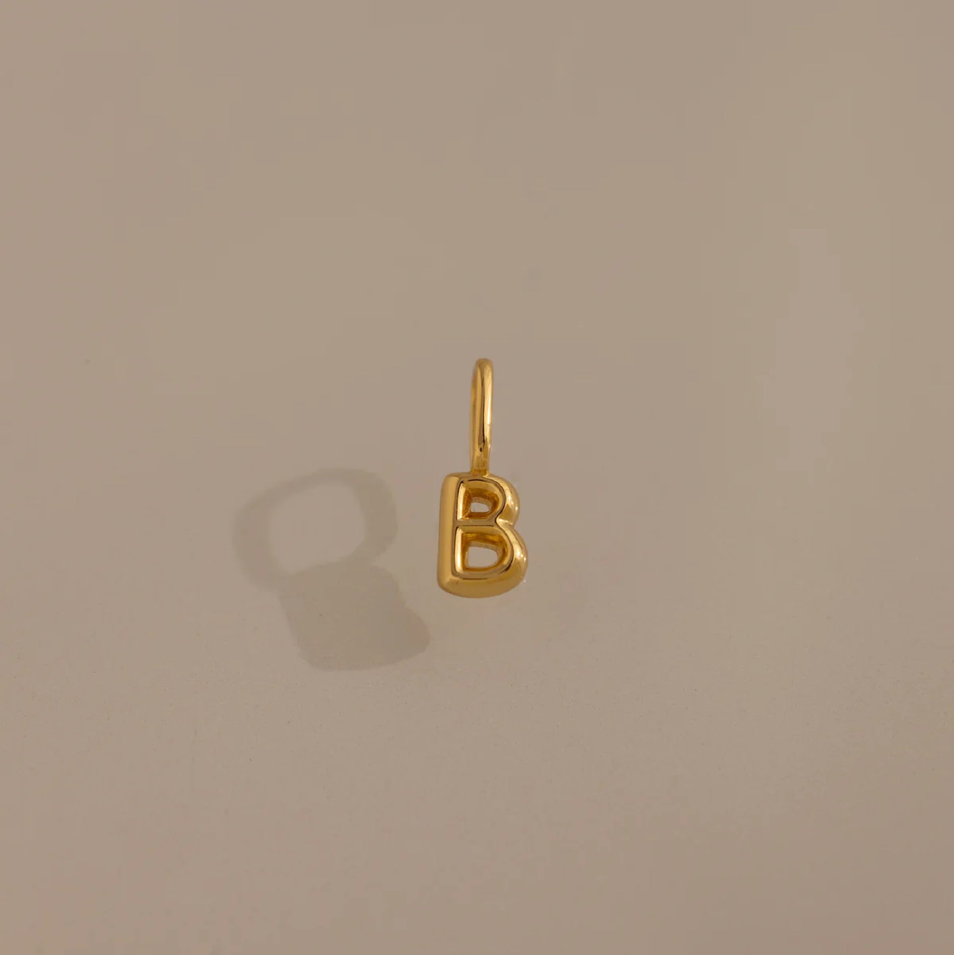 Gold letter 'B' charm on a beige background