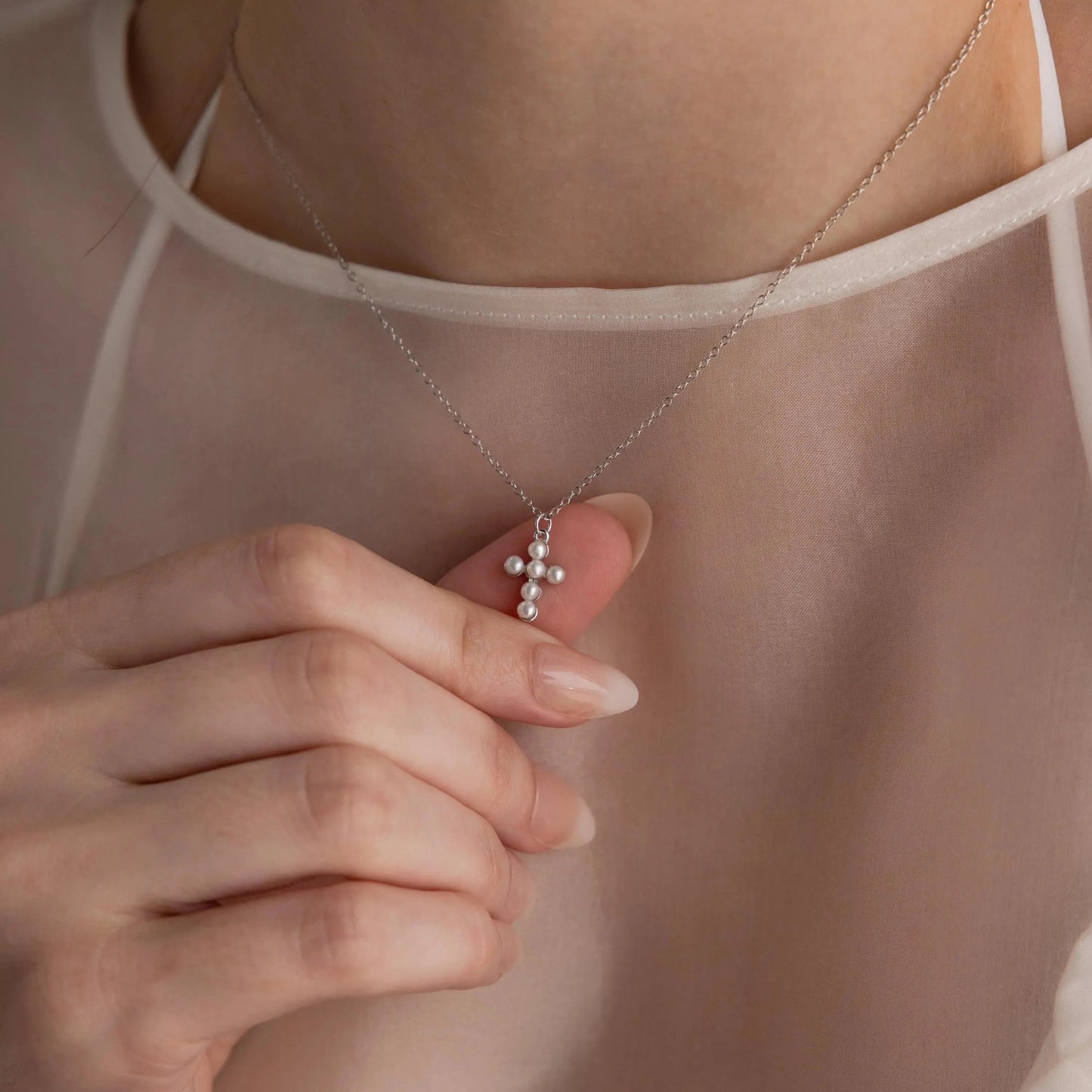 Necklace with a cross pendant held by a hand against a neutral background