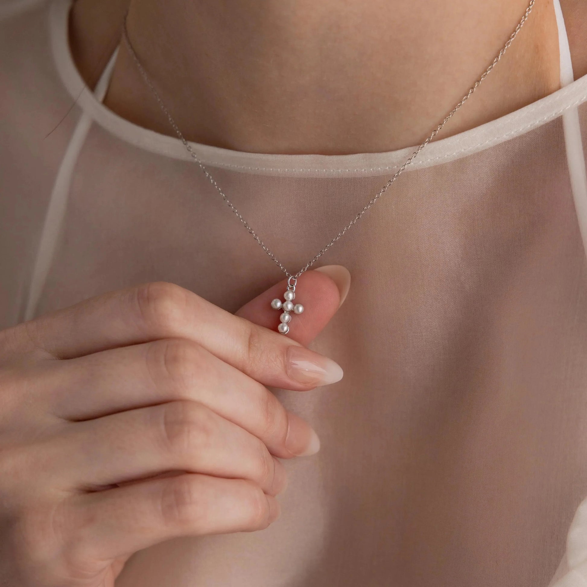 Necklace with a cross pendant held by a hand against a neutral background