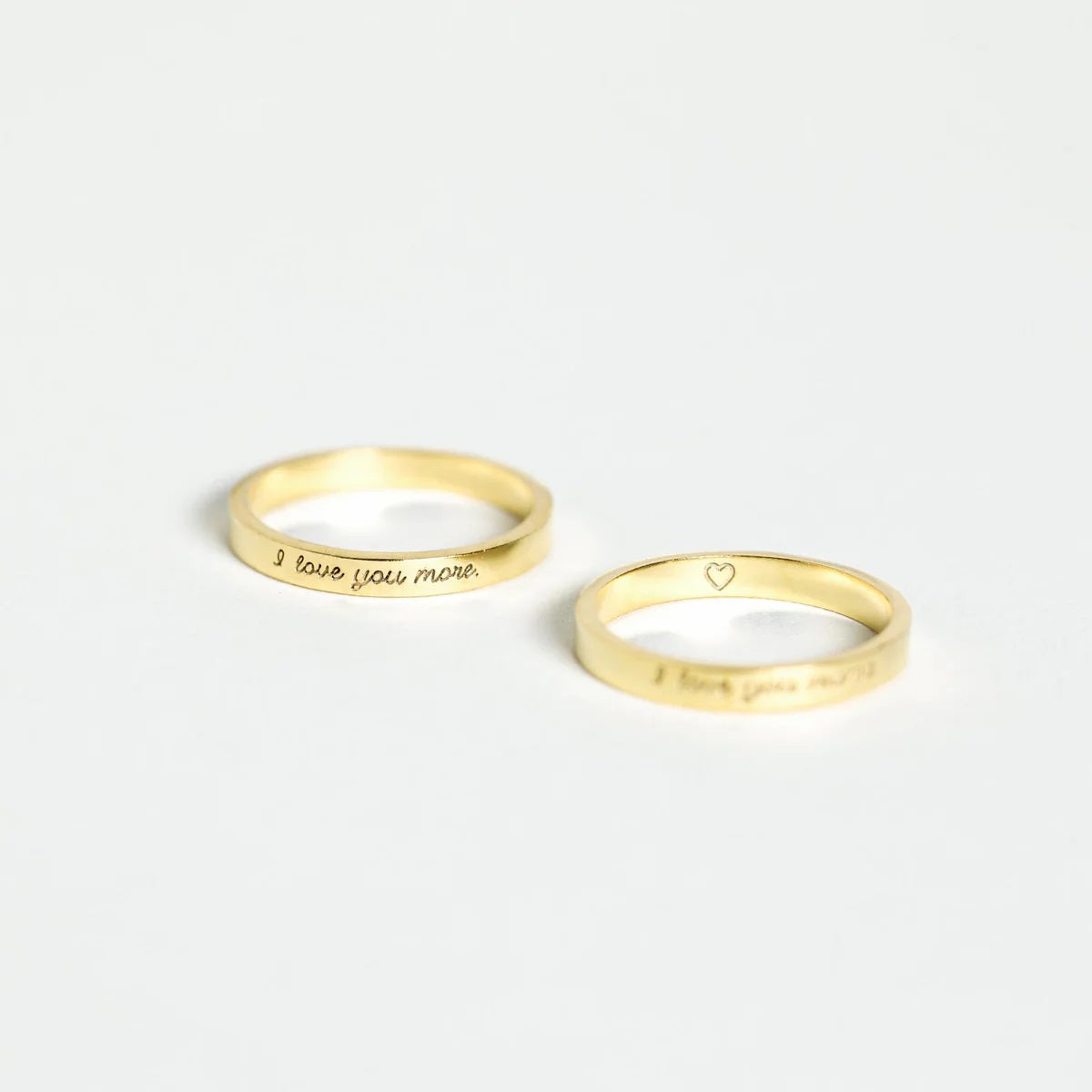 Two gold rings with engraved text on a white background