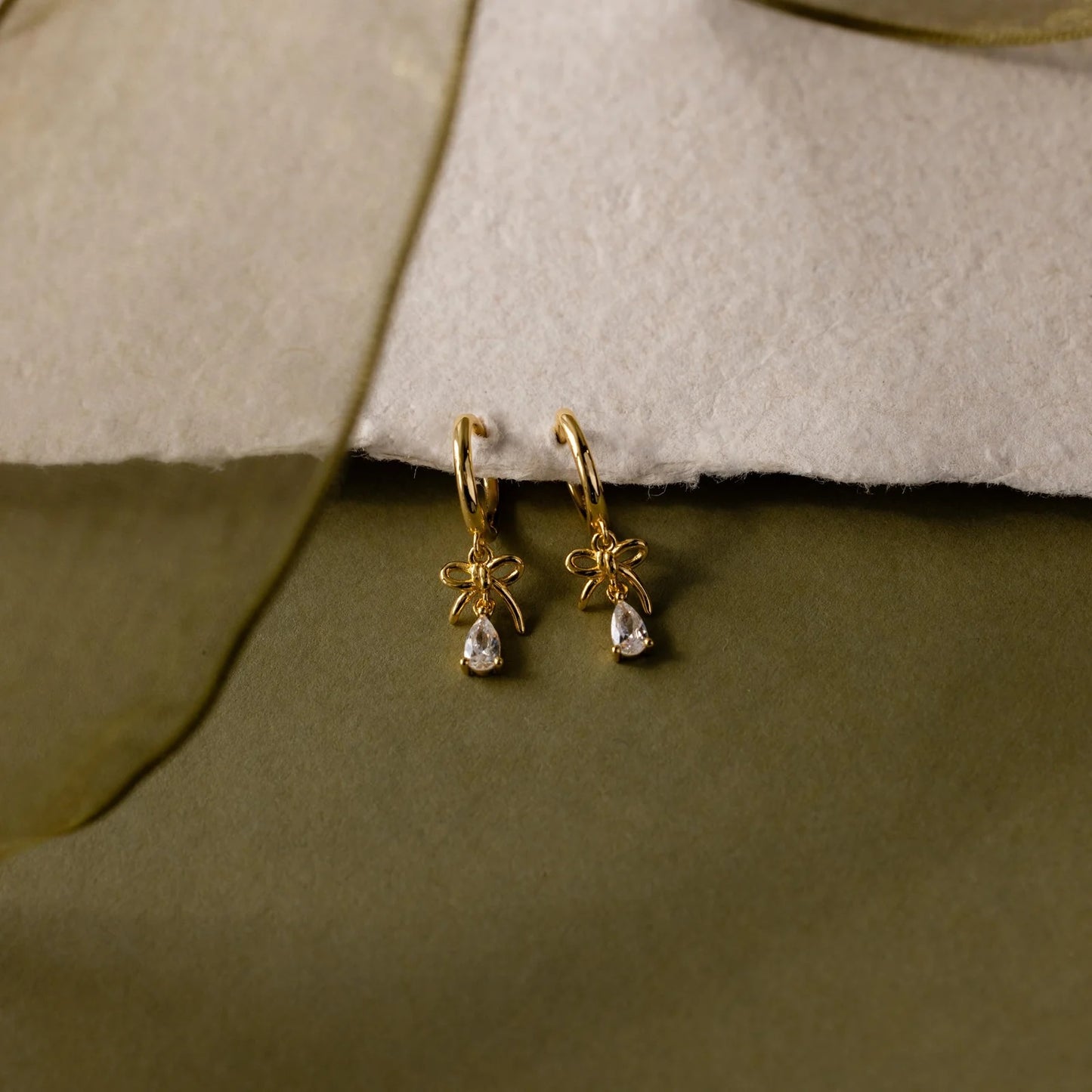 Gold earrings with teardrop-shaped stones on a textured surface