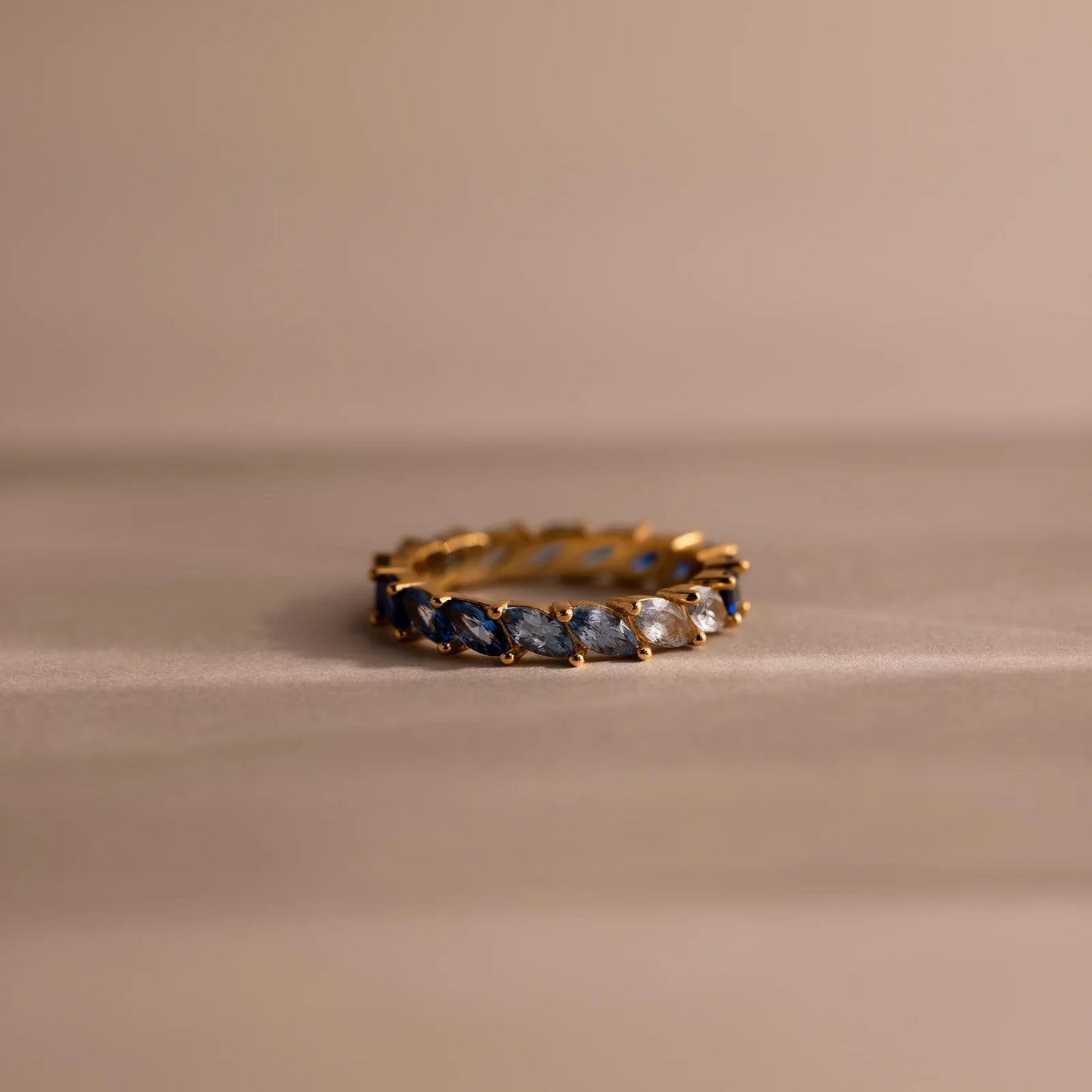 Gold ring with blue and white gemstones on a beige background