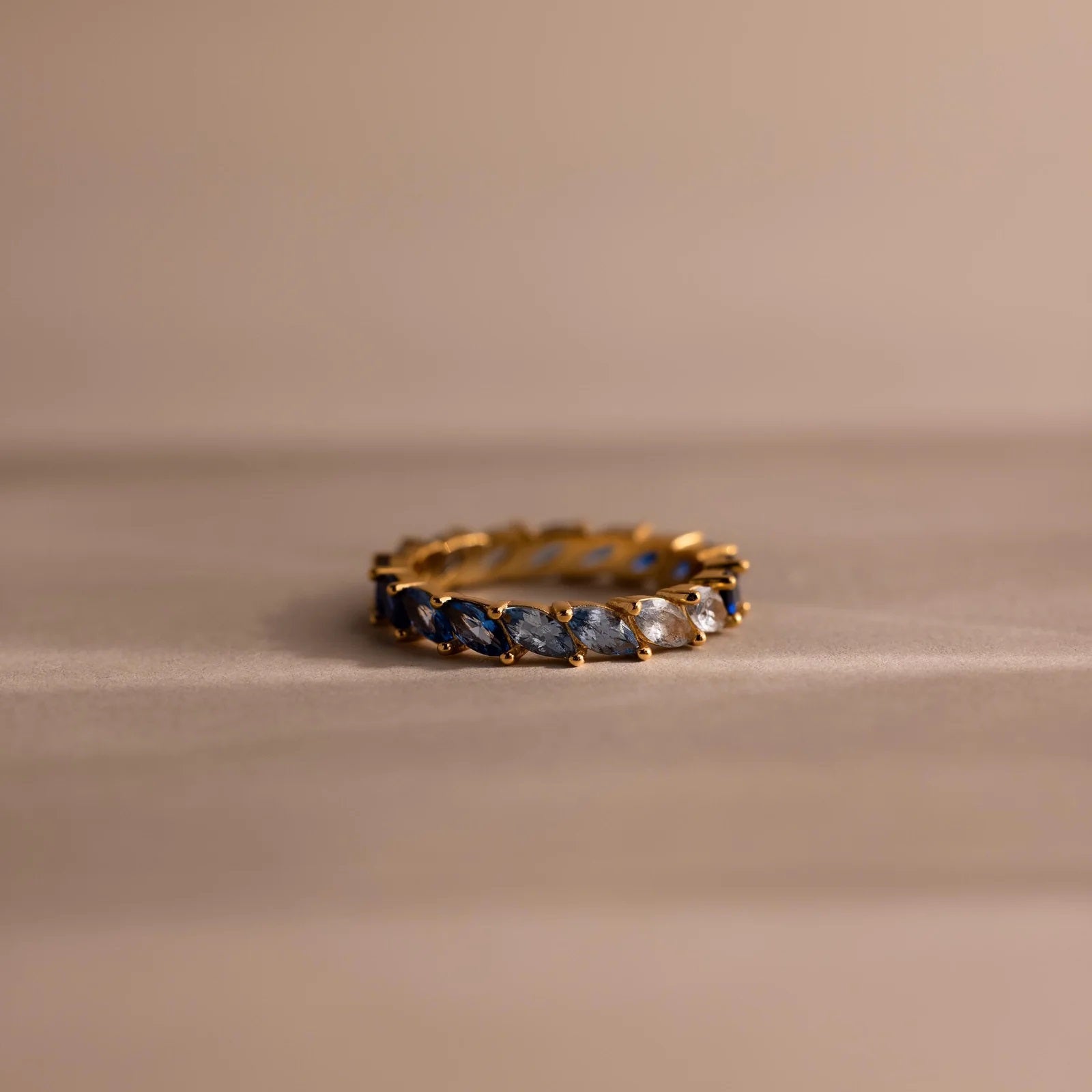 Gold ring with blue and white gemstones on a beige background
