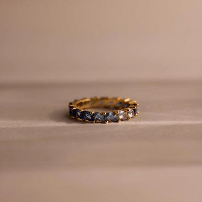 Gold ring with blue and white gemstones on a beige background