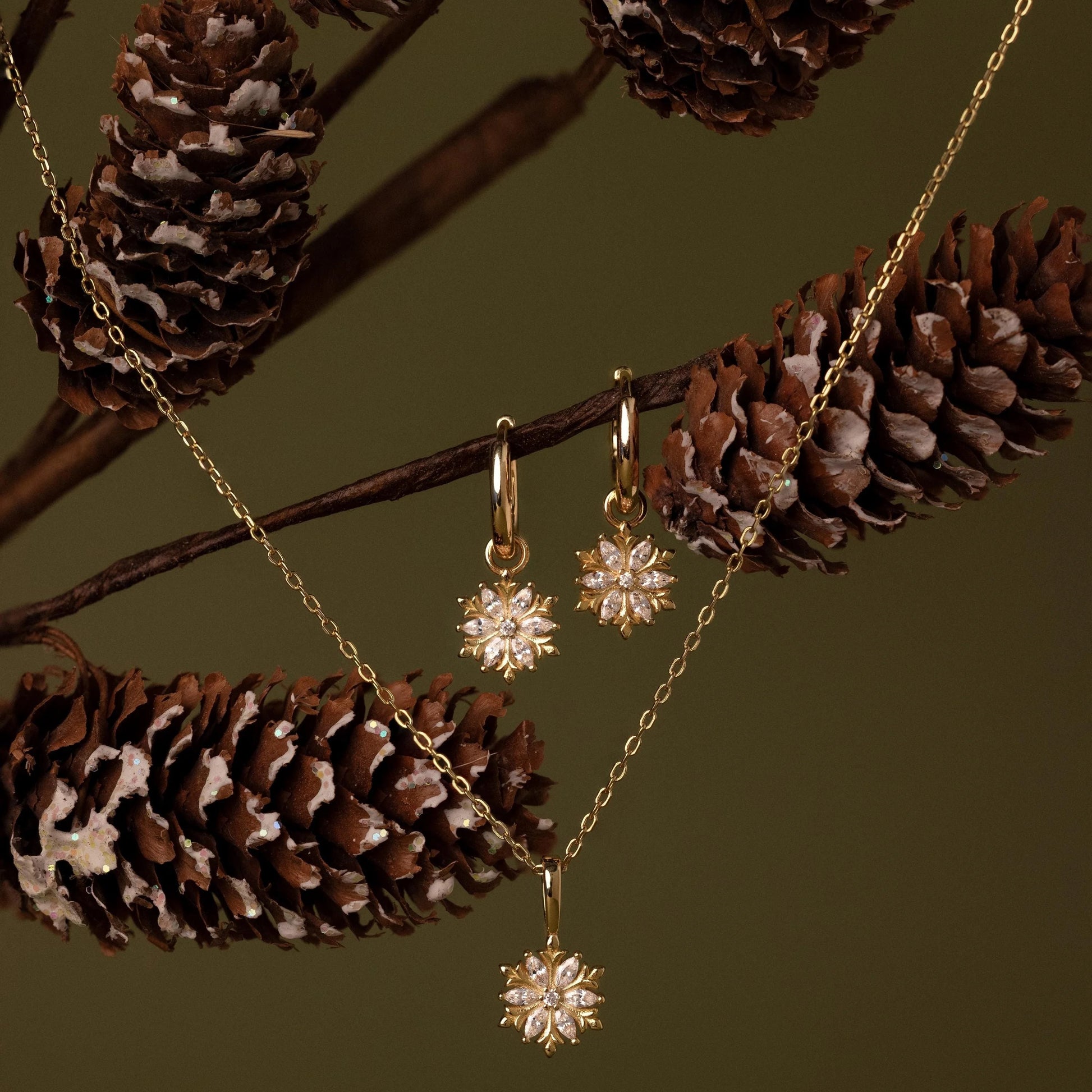 Gold jewelry set with star-shaped pendants on a branch with pine cones
