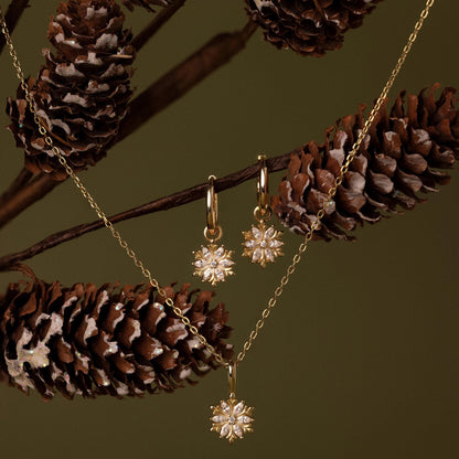 Gold jewelry set with star-shaped pendants on a branch with pine cones