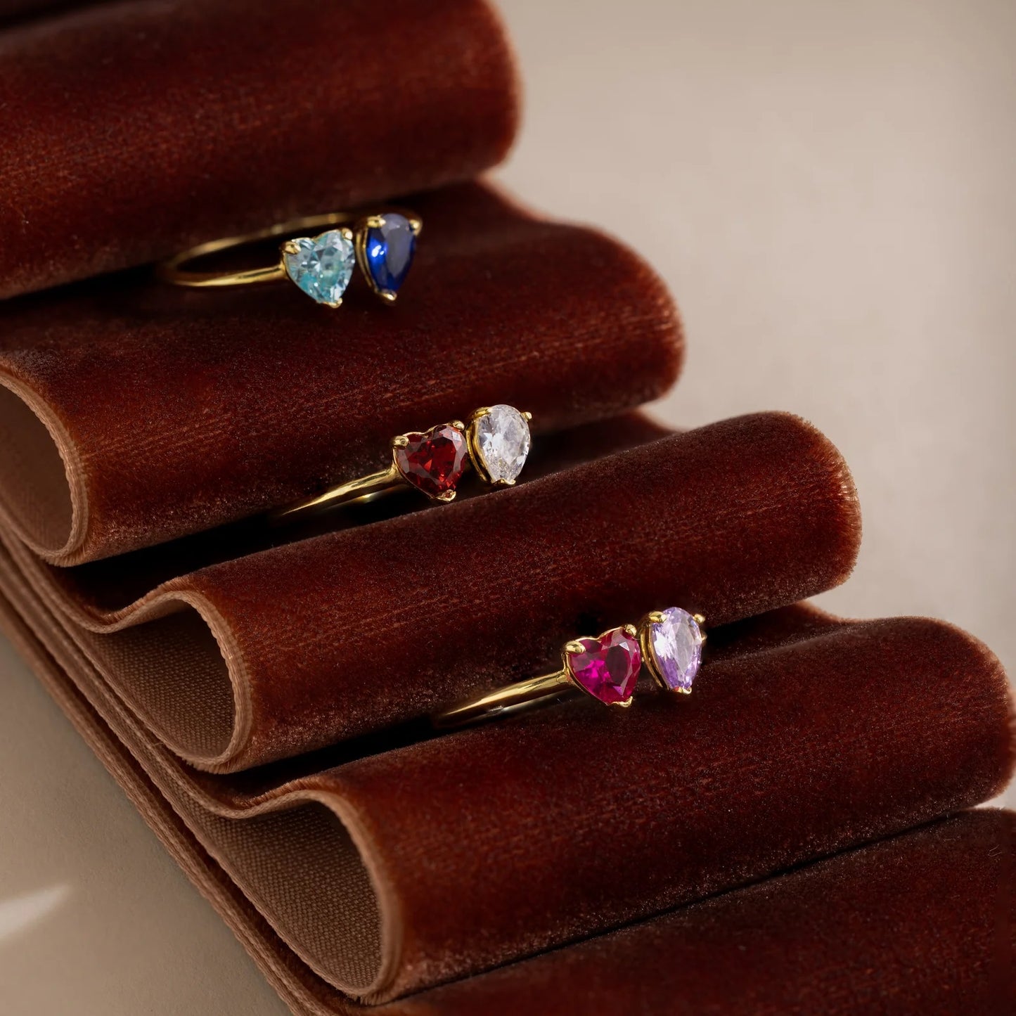 Set of heart-shaped gemstone rings on a brown velvet stand