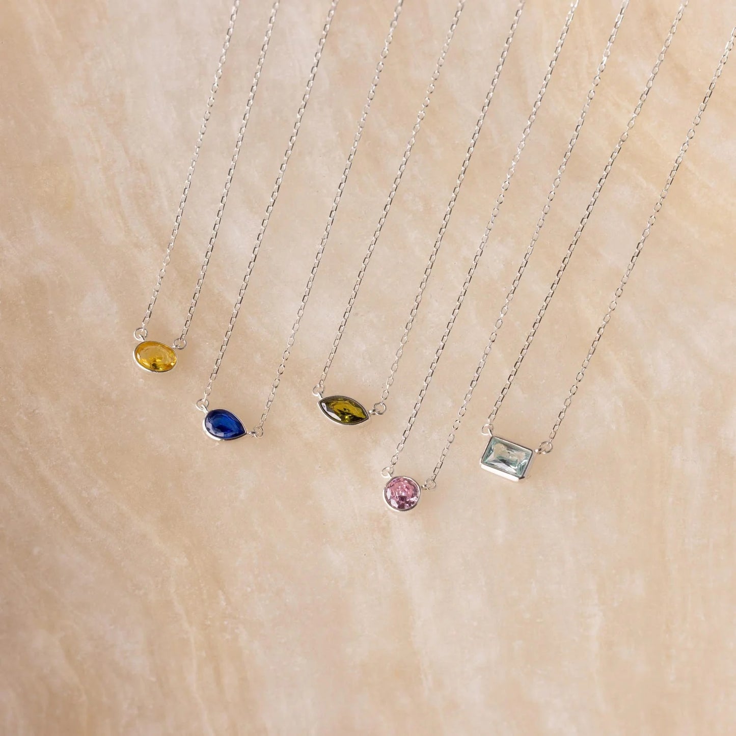 Four necklaces with different colored gemstones on a beige surface