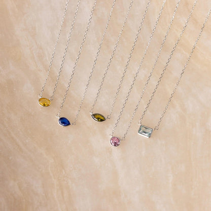 Four necklaces with different colored gemstones on a beige surface