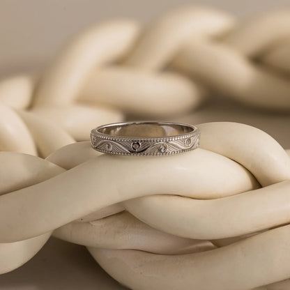 Silver ring with intricate design on a braided beige rope background