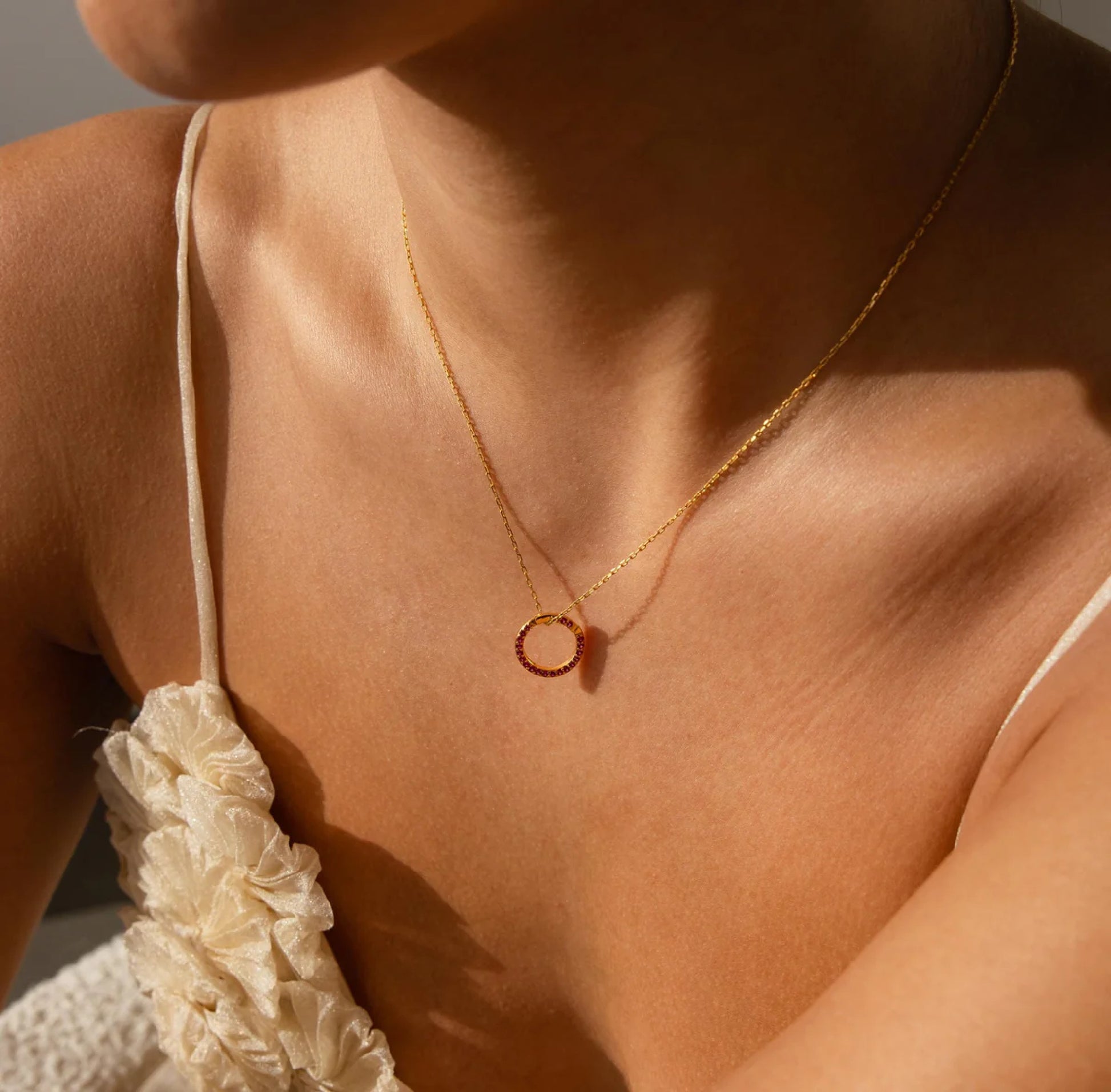 Close-up of a person wearing a gold necklace with a circular pendant.