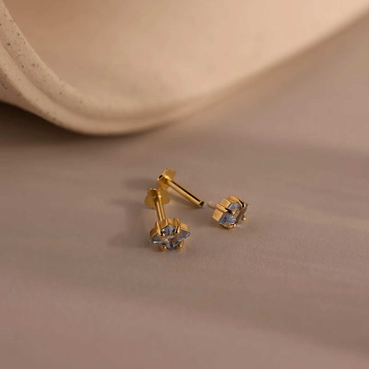 Gold earrings with blue gemstones on a beige surface
