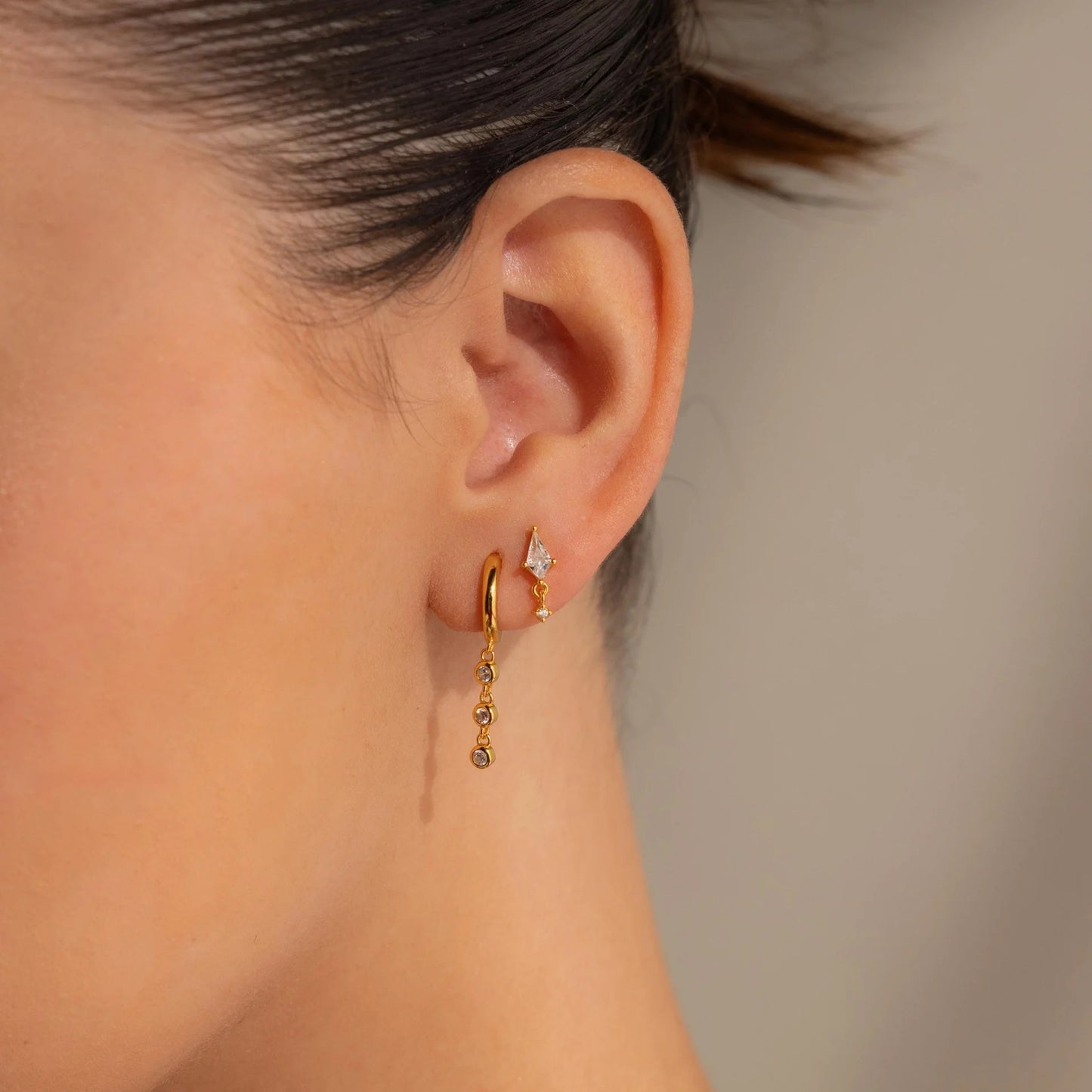 Close-up of a person wearing gold hoop earrings with a neutral background