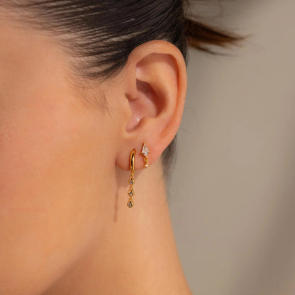 Close-up of a person wearing gold hoop earrings with a neutral background