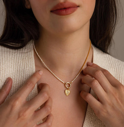 Close-up of a person wearing a gold necklace with a heart-shaped pendant.