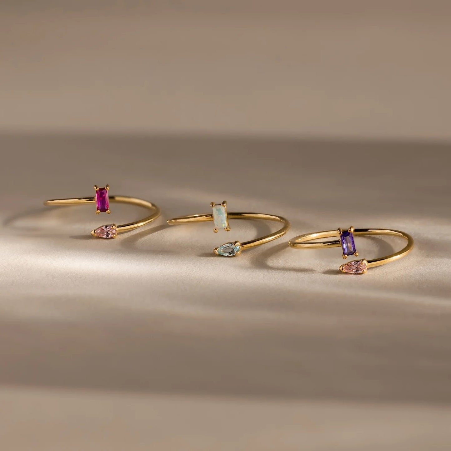 Three gold bangle bracelets with gemstones on a neutral background