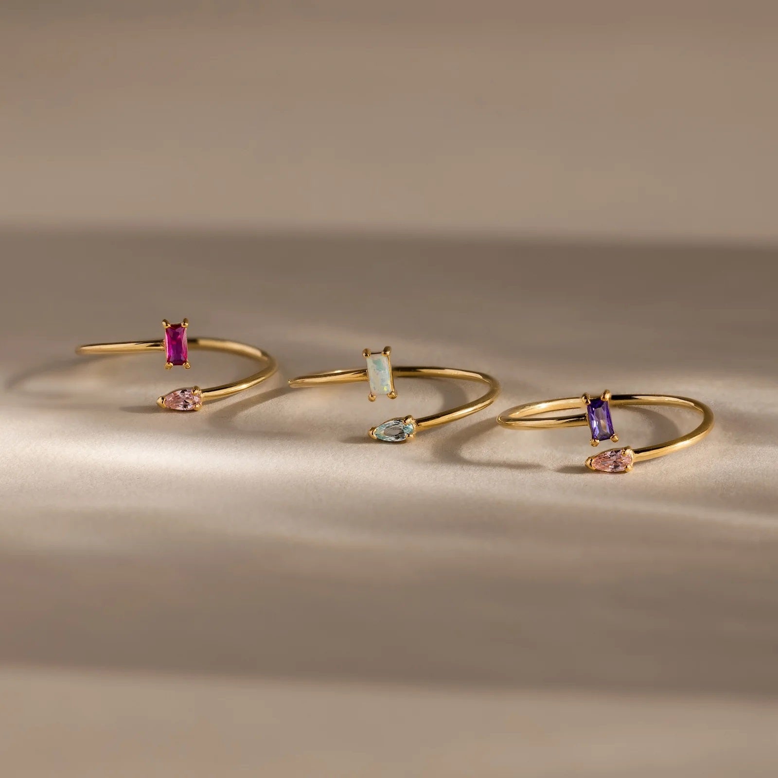 Three gold bangle bracelets with gemstones on a neutral background