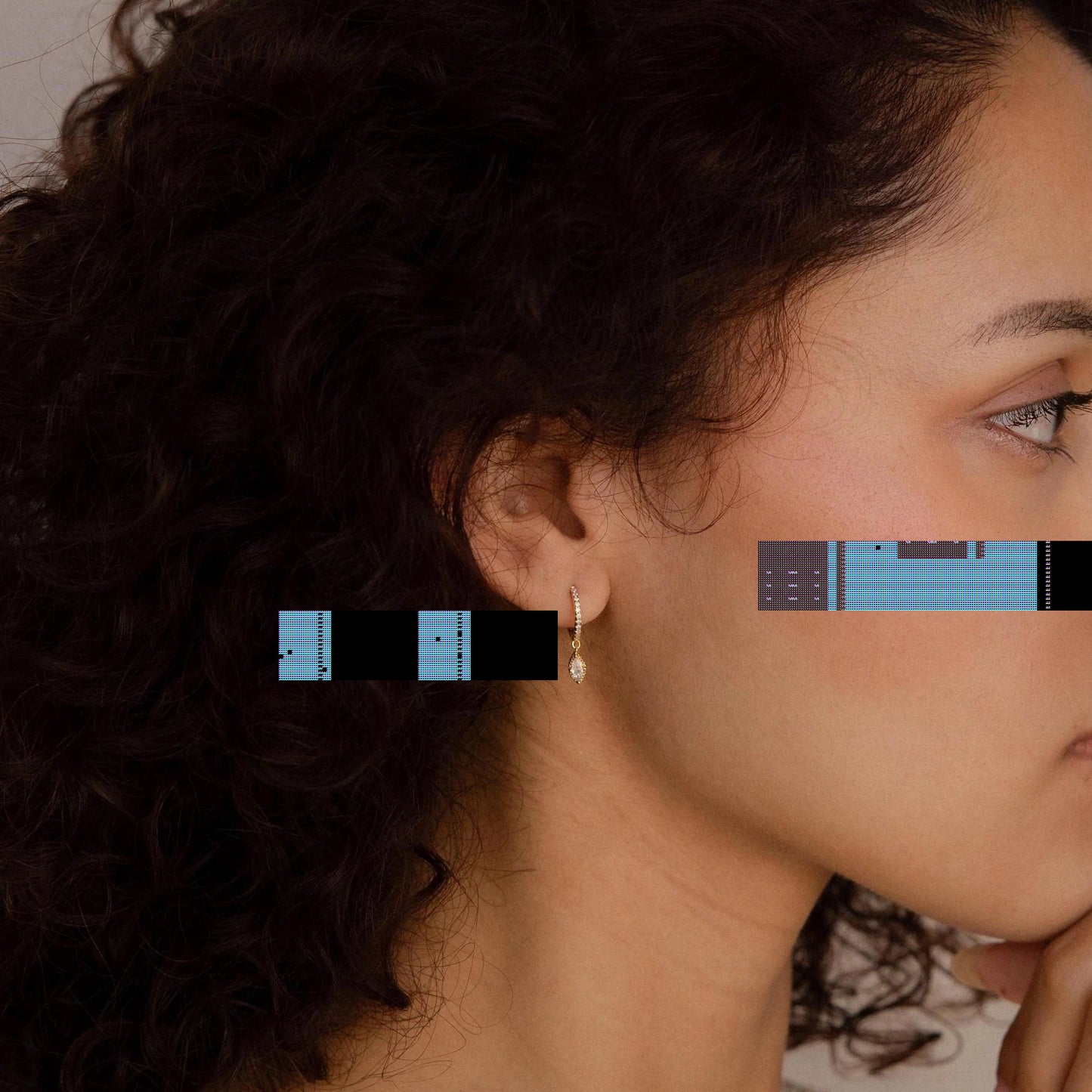 Woman with curly hair wearing a delicate earring against a neutral background