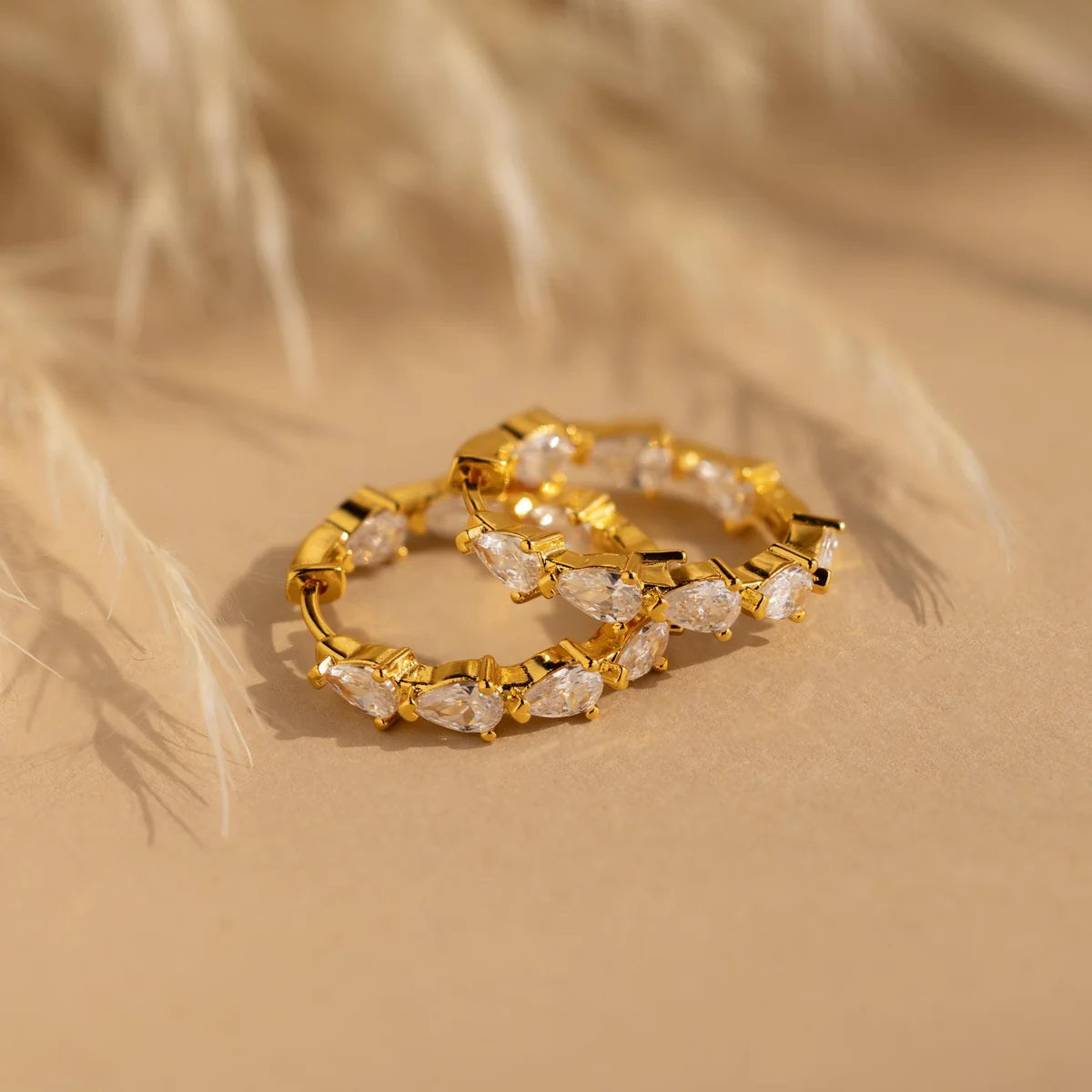 Gold hoop earrings with clear stones on a beige background