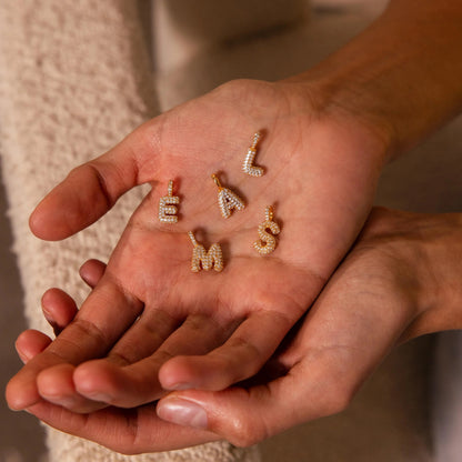 Gold letter-shaped jewelry pieces on a person's palm