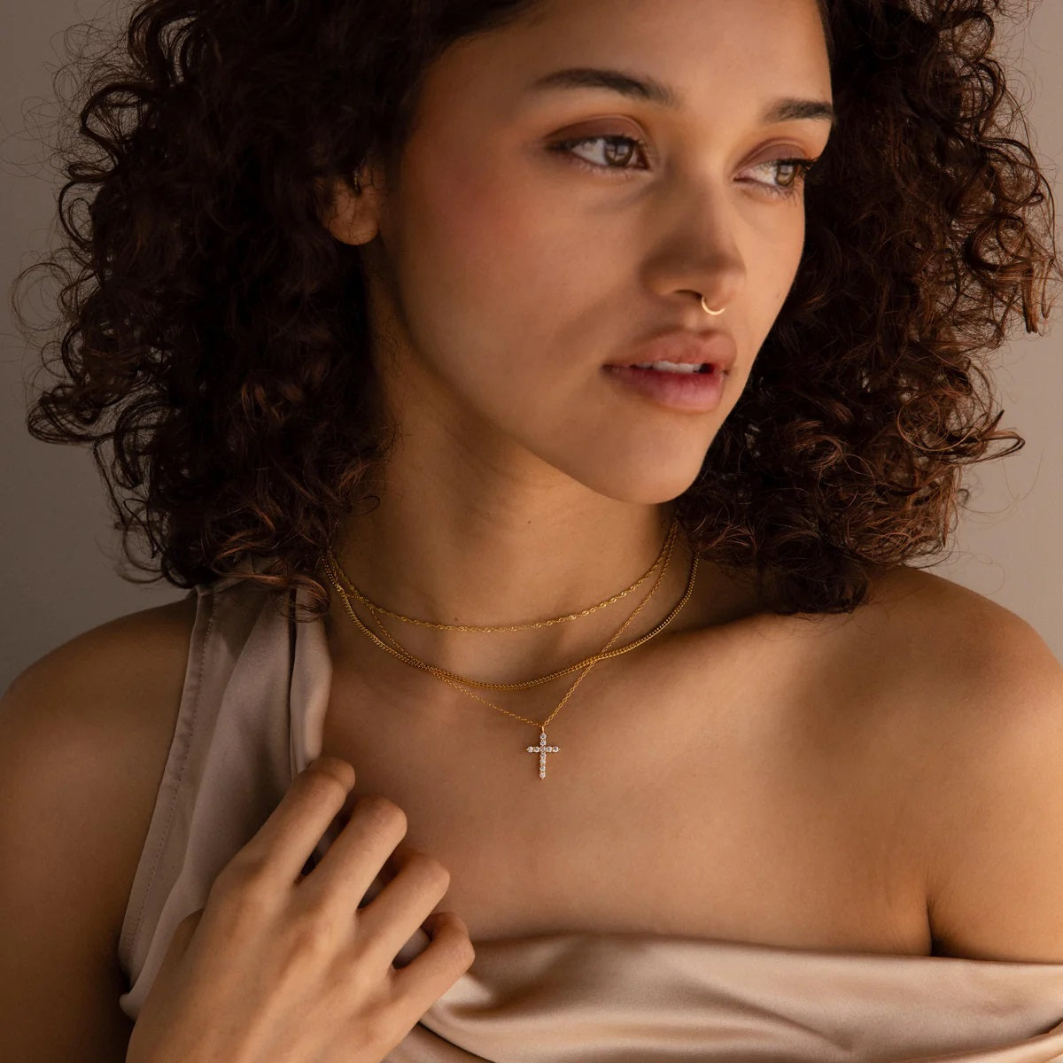Woman wearing a gold necklace with a cross pendant against a neutral background