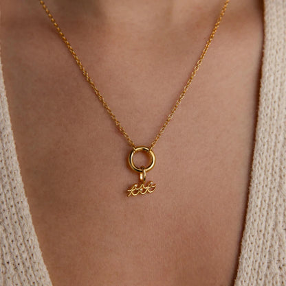 Gold necklace with a pendant on a person wearing a beige cardigan.