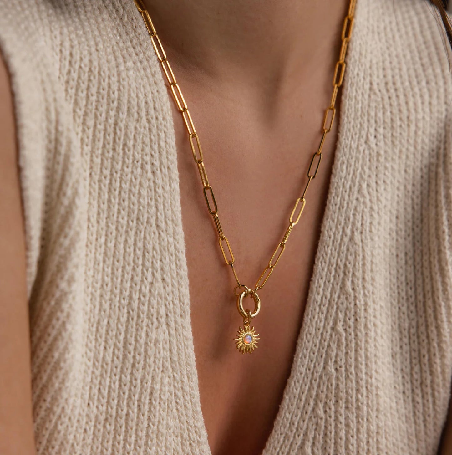 Gold chain necklace with a sun pendant worn by a person in a beige sweater.