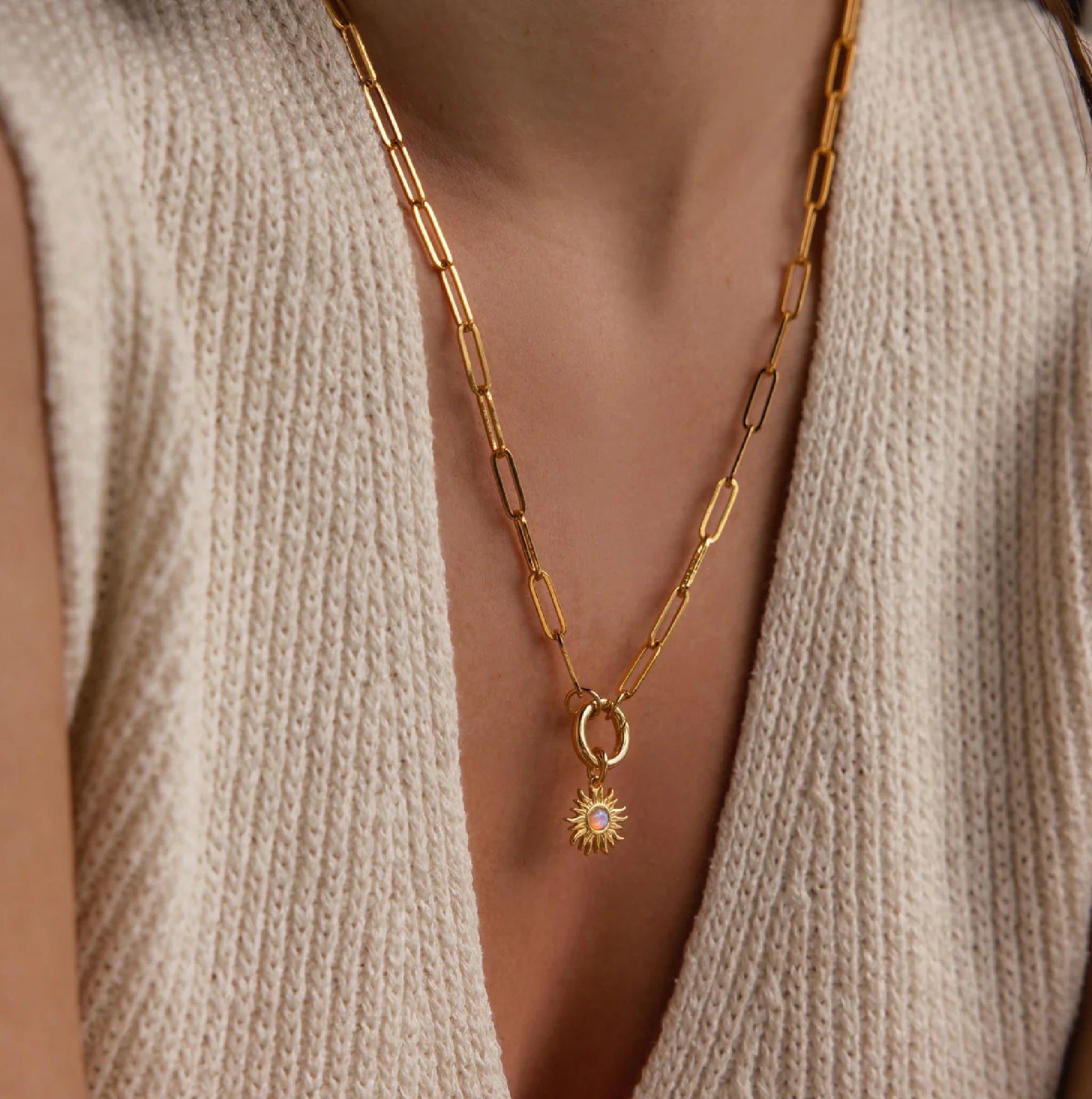 Gold chain necklace with a sun pendant worn by a person in a beige sweater.