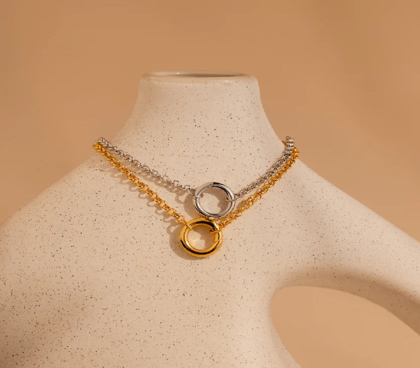 Two gold and silver necklaces on a mannequin bust against a beige background