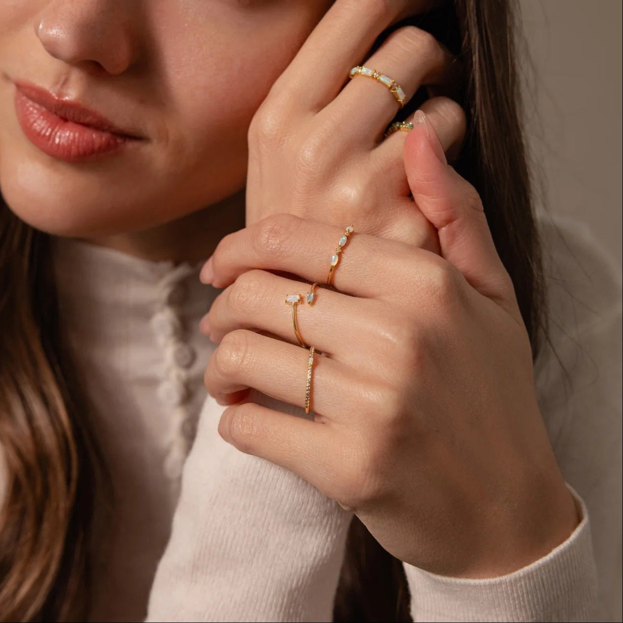 Woman wearing multiple gold rings on a neutral background
