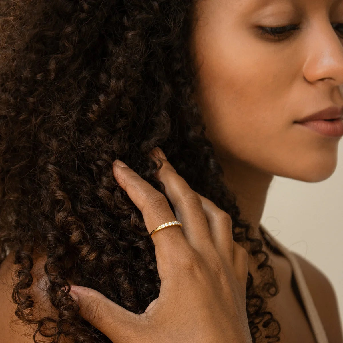 Close-up of a woman's hand touching her curly hair with a neutral background