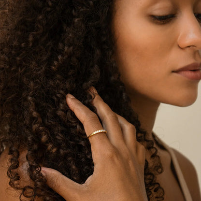 Close-up of a woman's hand touching her curly hair with a neutral background