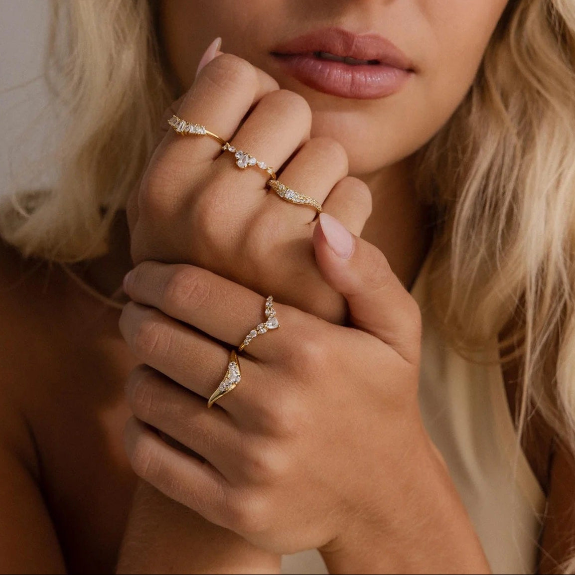 Woman wearing multiple diamond rings on a neutral background