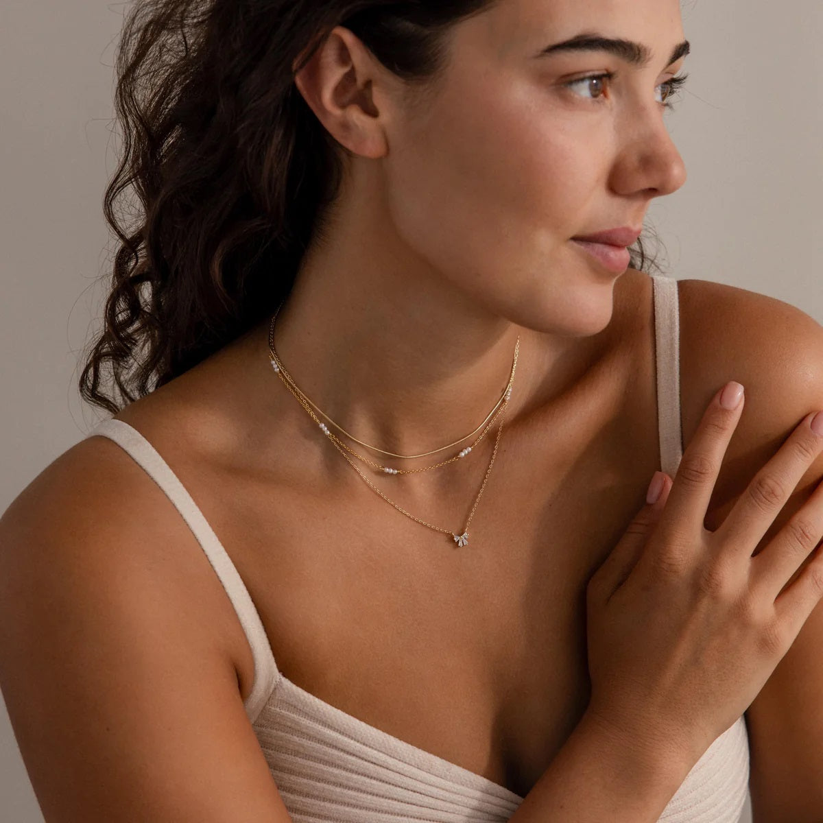 Woman wearing a delicate gold necklace with a neutral background